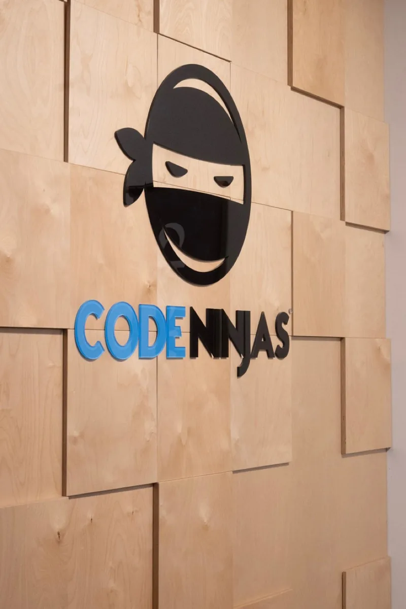 The Code Ninjas sign on a wood panel wall.