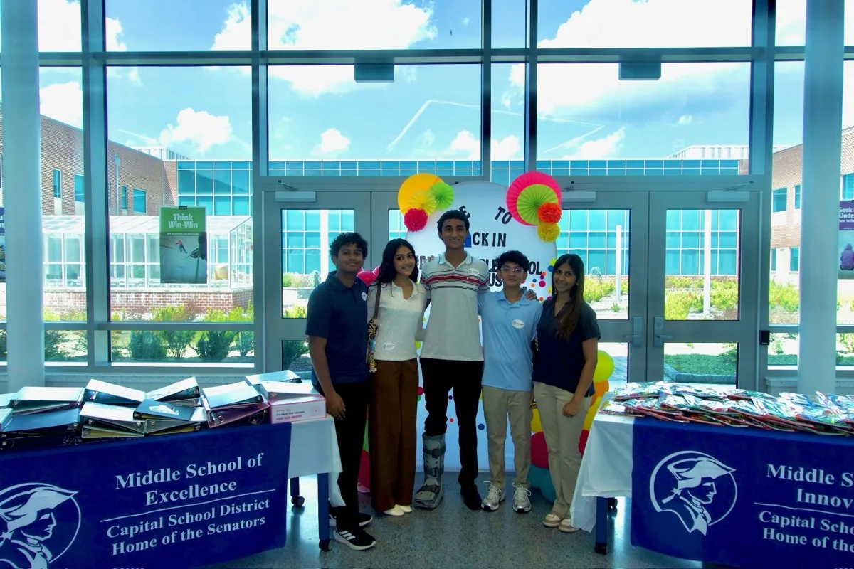The SkillSphere team behind a table of packed supply kits at the Dover Middle School campus, windows and balloons behind them.