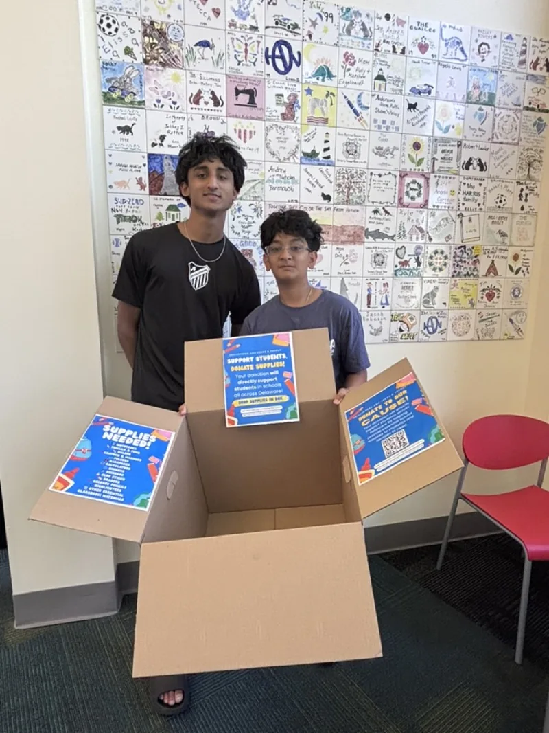 Two SkillSphere students holding a donation box in front of a mural.