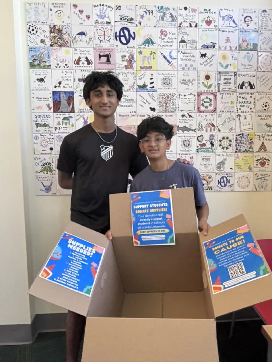 Two students holding an open donation box with SkillSphere flyers taped to it.