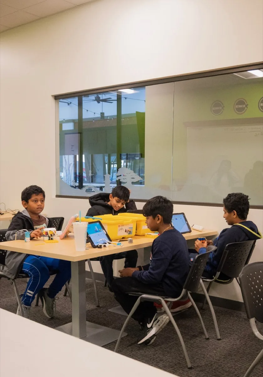 Middle school students at a table working on laptops next to LEGO SPIKE kits.