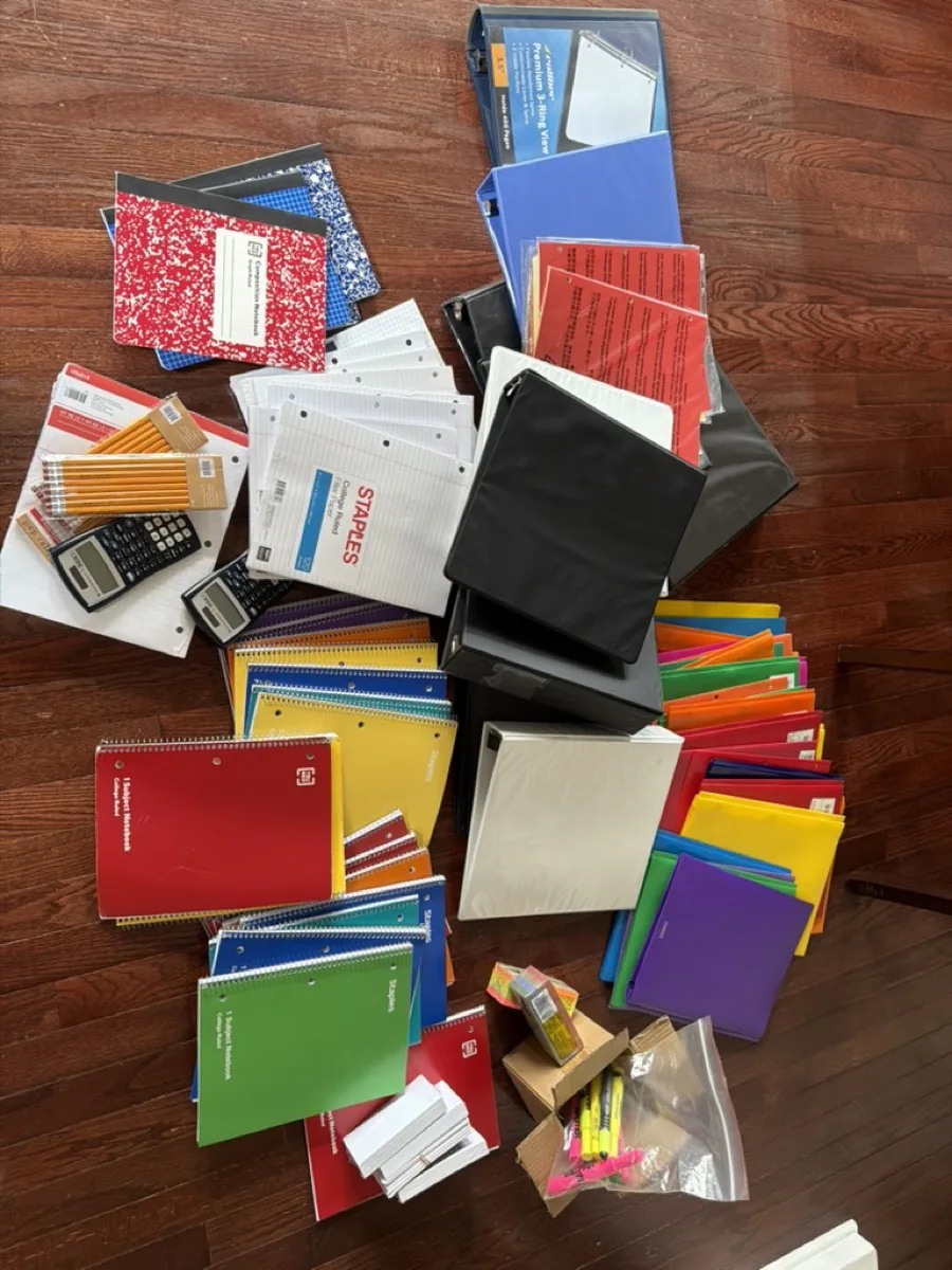 School supplies spread across a wood floor: notebooks, folders, pencils, calculators, and binders.