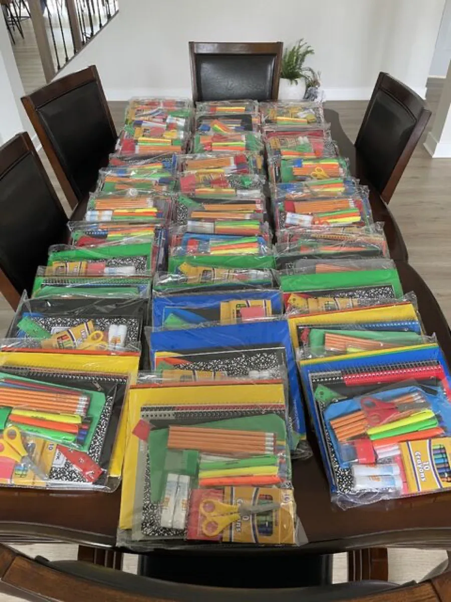Dozens of packed school supply kits laid out across a long table, each with notebooks, pencils, folders, and scissors.